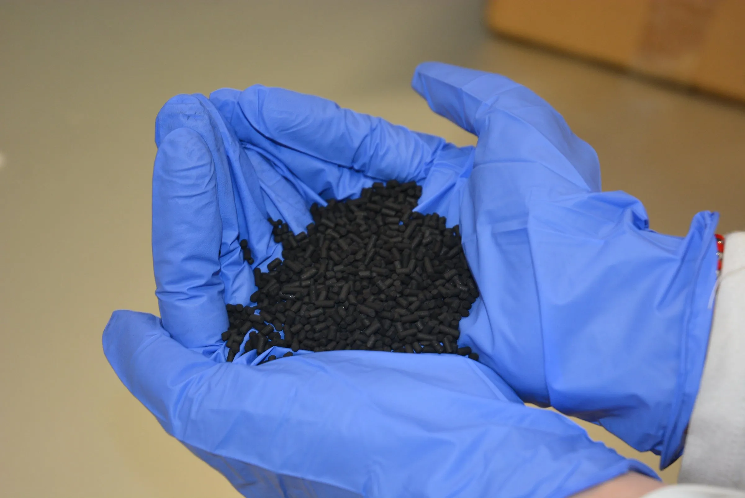 Gloved hands holding a pile of black adsorbent pellets